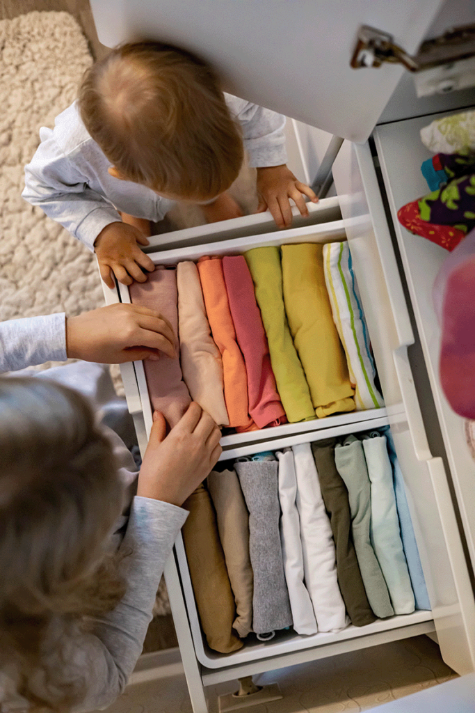 A child and a toddler open up a drawer of well organized and folded clothes.